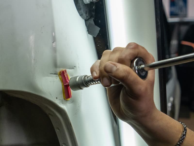 Technician pulling a small door dent with a paintless dent repair glue tab